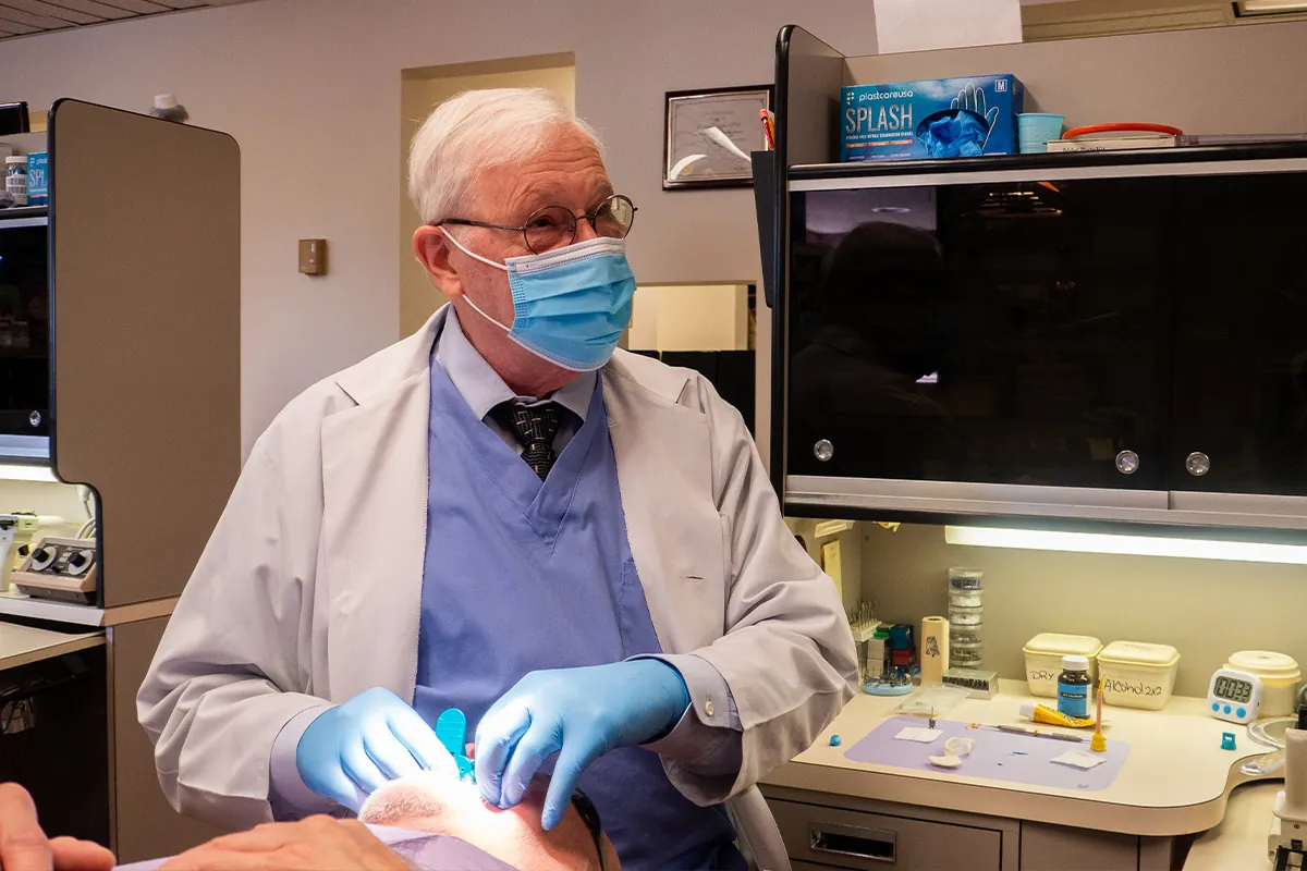 Dr. Hughes crafting a male patient dentures while speaking to dental assistant